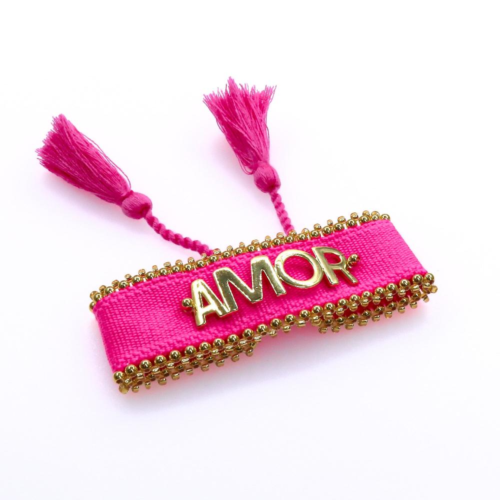Pink fabric AMOR bracelet with gold bead accents and tassel ends, handcrafted with love.