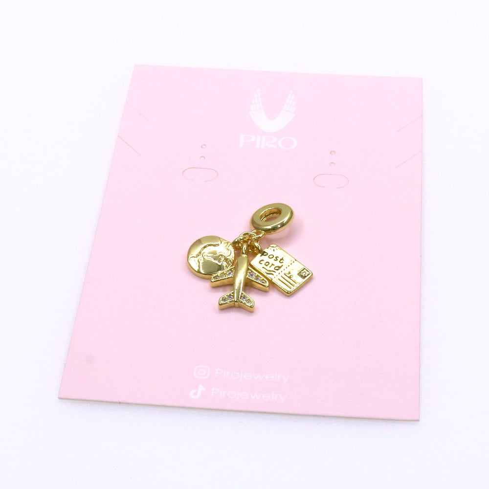 Gold travel charm featuring a globe, airplane, and postcard on a pink card background