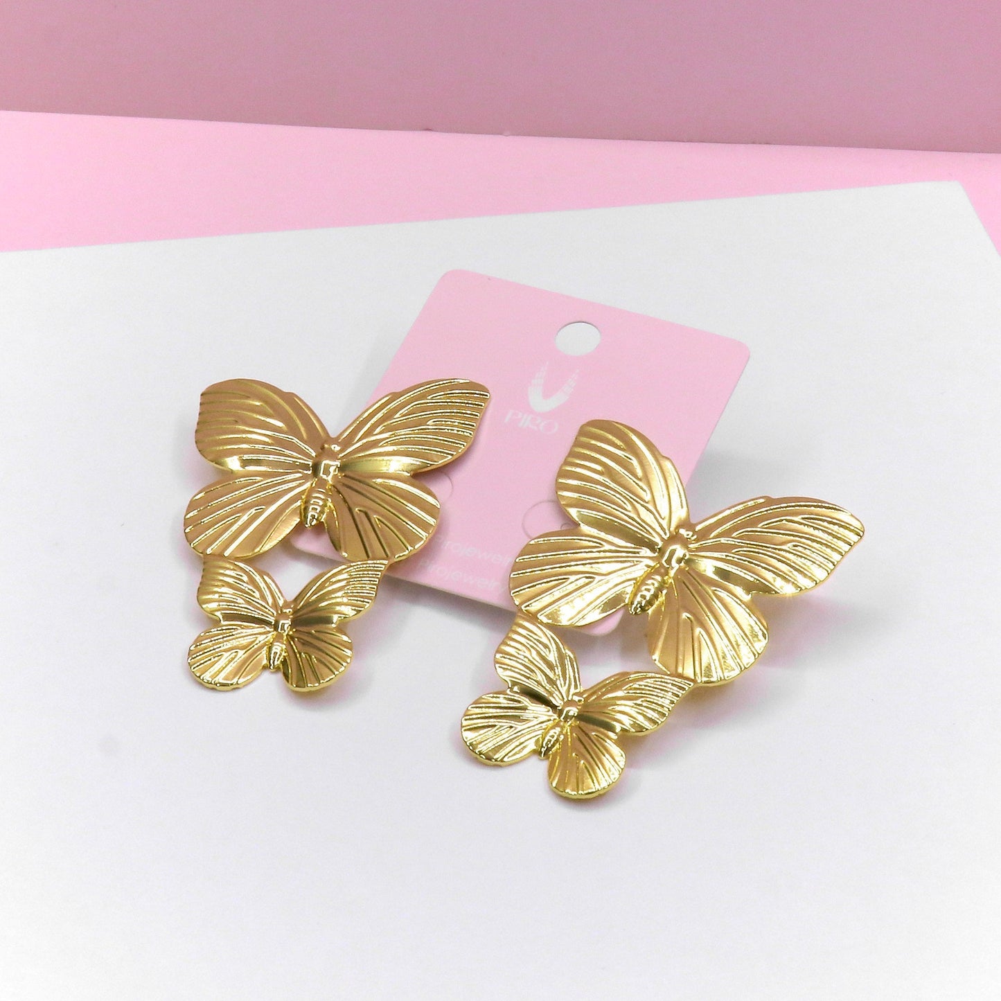 Pair of gold double butterfly earrings with intricate wing details on a pink card background