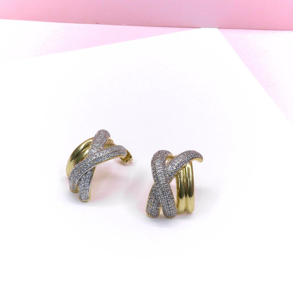 Pair of X-shaped chunky gold and silver earrings with textured design on a white and pink background