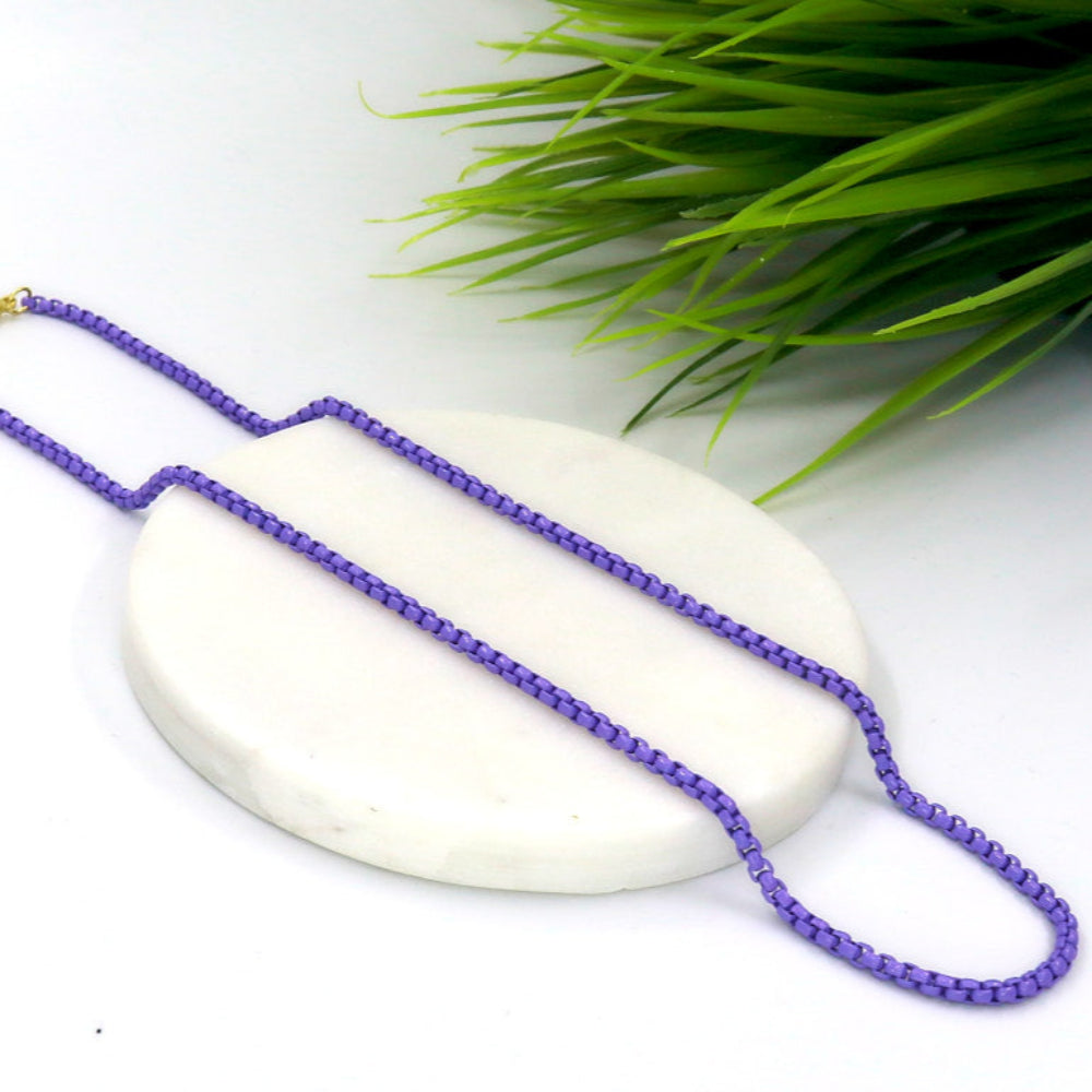 Purple stainless steel candy chain laid on a round white marble platform with green plant in the background
