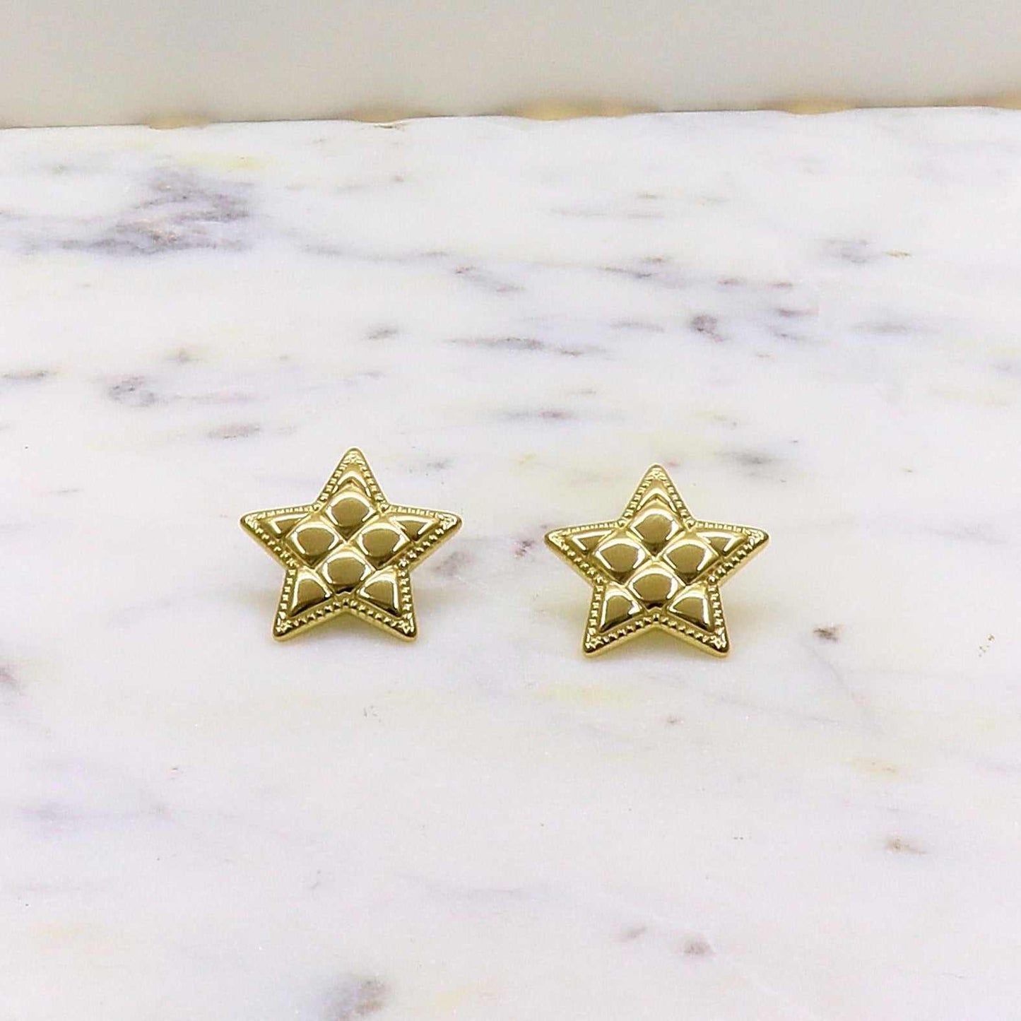 Gold-colored stainless steel star-shaped Estrella Fugas earrings on a marble surface