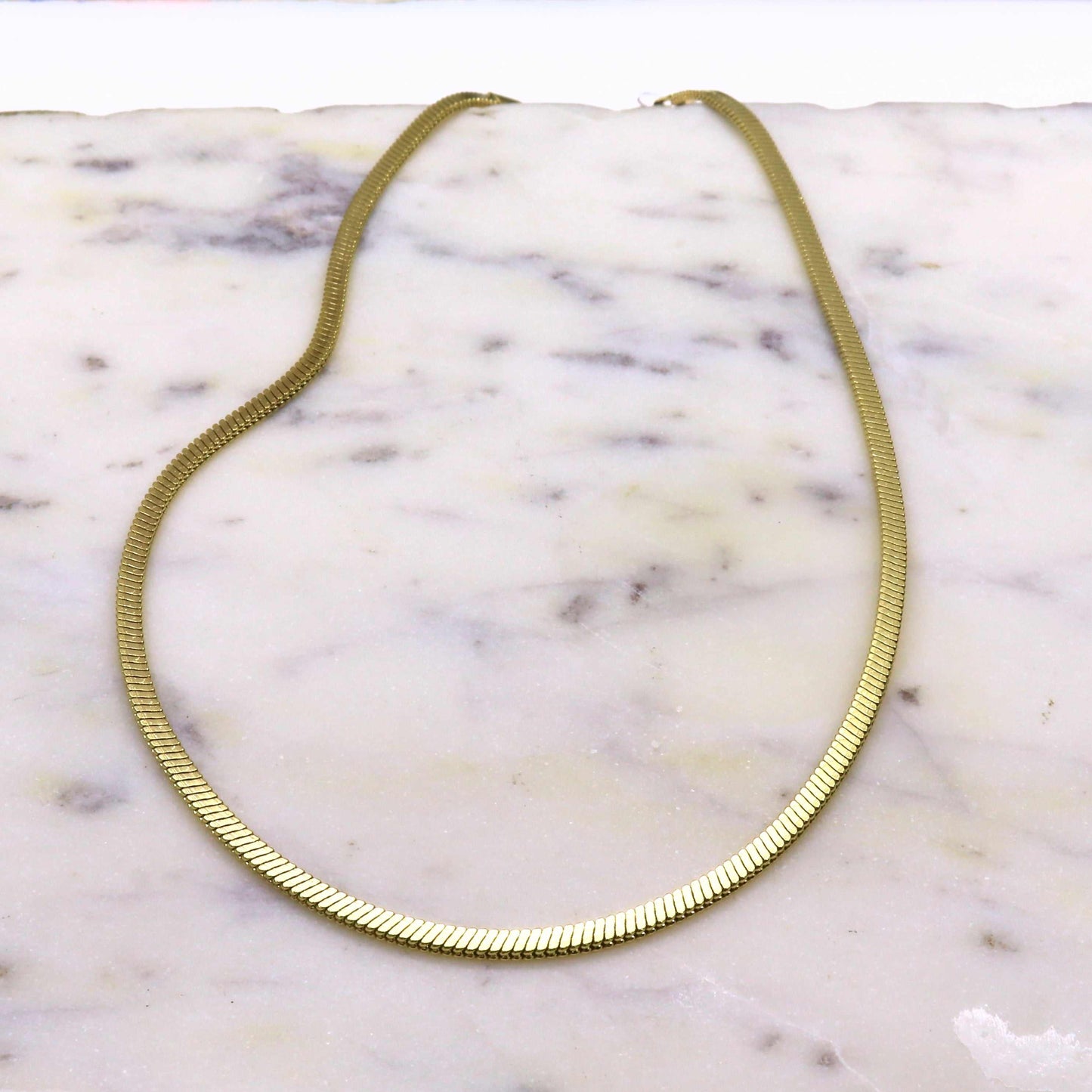 Gold-colored stainless steel herringbone link necklace on marble background