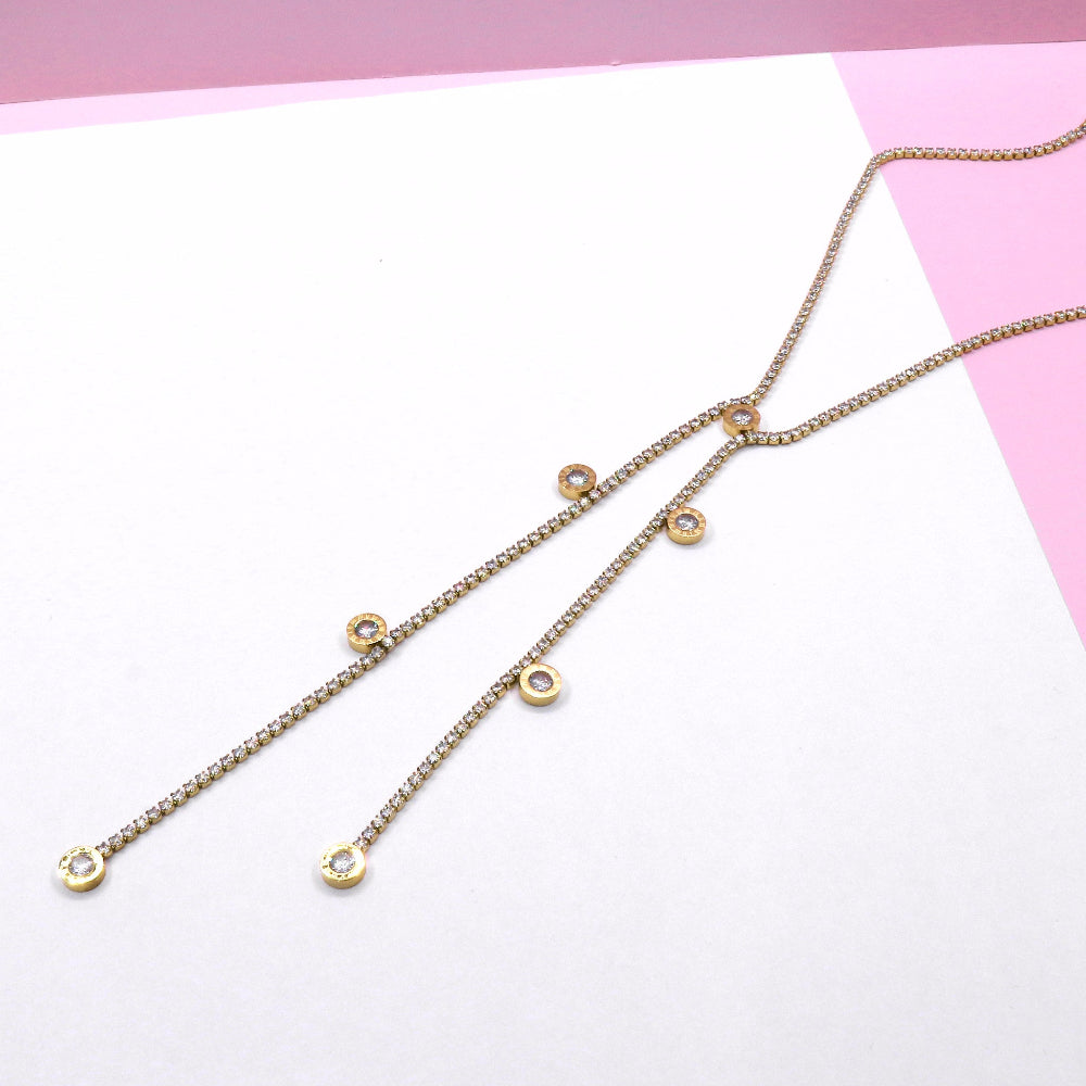 Long delicate gold tennis chain with small round pendants on a pink and white background