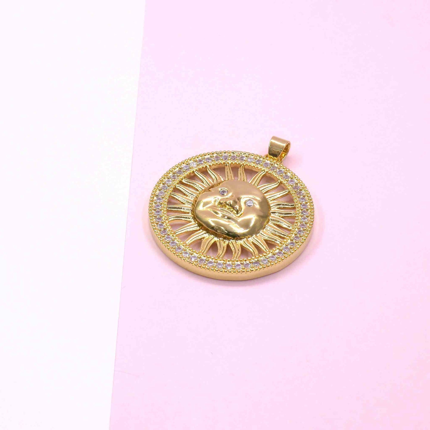 Gold Mother Sun Charm pendant with zirconia accents and intricate sun design on pink background
