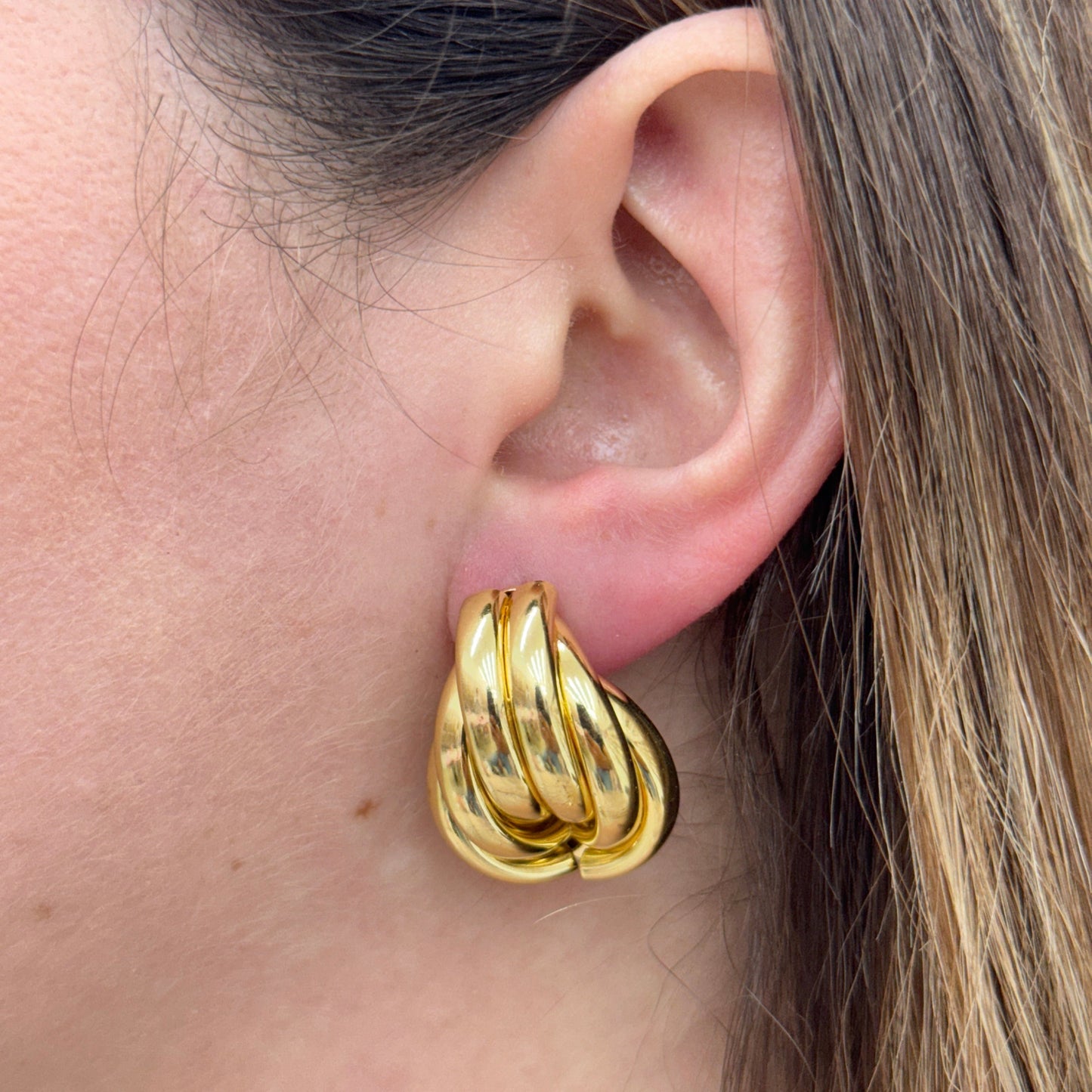 Close-up of an ear wearing a gold half knot earring with a twisted design