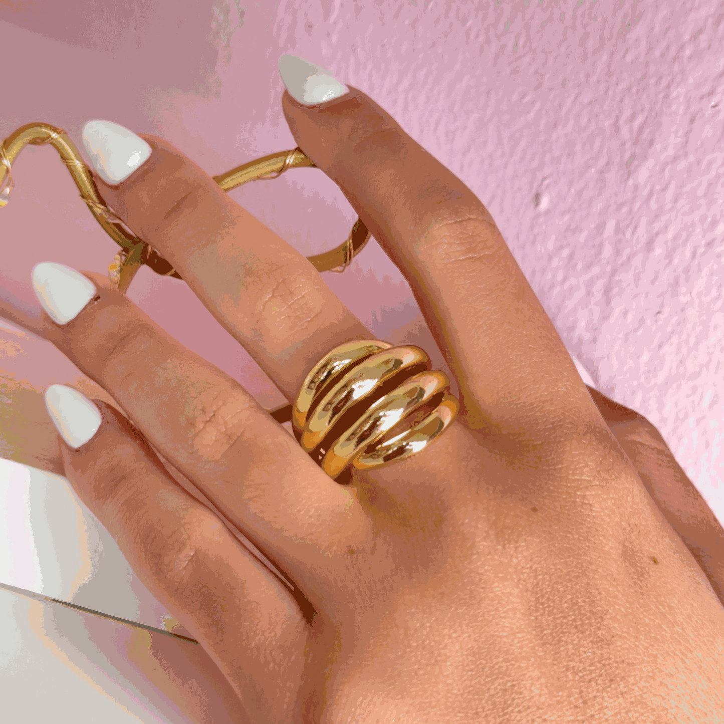 Gold spiral ring worn on hand with white manicure against pink background