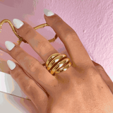 Gold spiral ring worn on hand with white manicure against pink background
