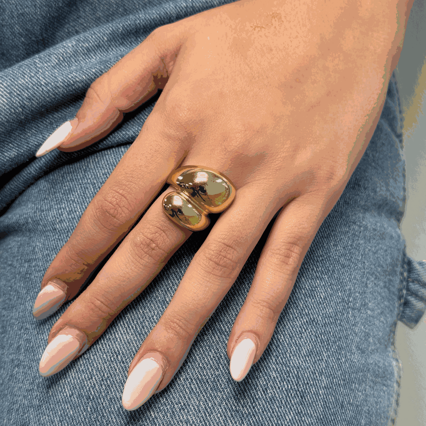 Hand wearing adjustable double drop style gold ring on denim background