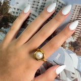 Gold-colored Mother Pearl Ring with a central pearl on a hand with white nails.