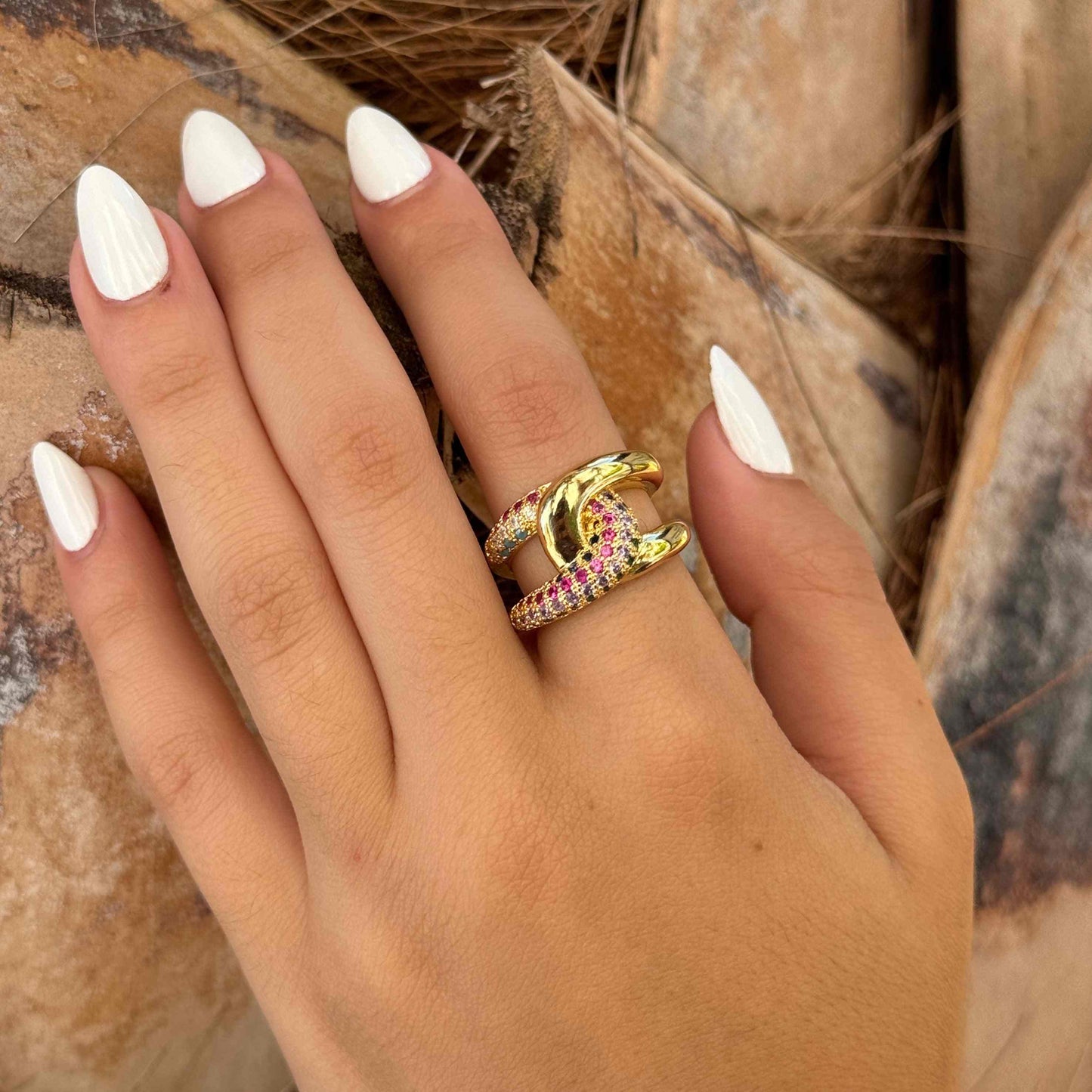 Hand wearing LINK GOLD RNG adjustable gold chain link ring with crystal accents and white nail polish on natural background