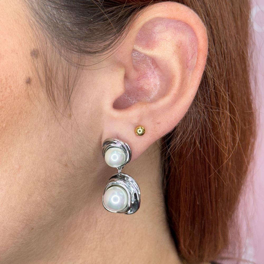 Close-up of an ear wearing elegant silver and gold 2 pearl long earrings.