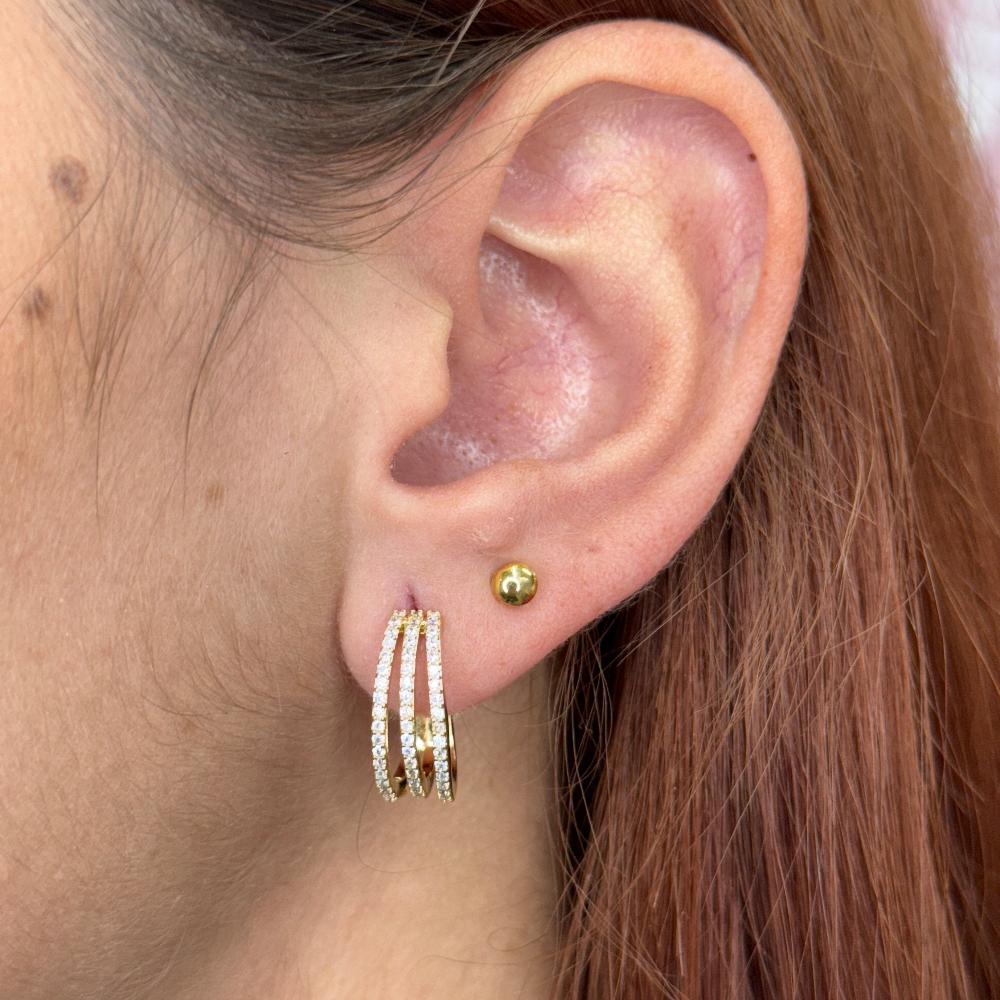 Close-up of an ear wearing trio gold hoop earrings with a triple line design and small gold stud.