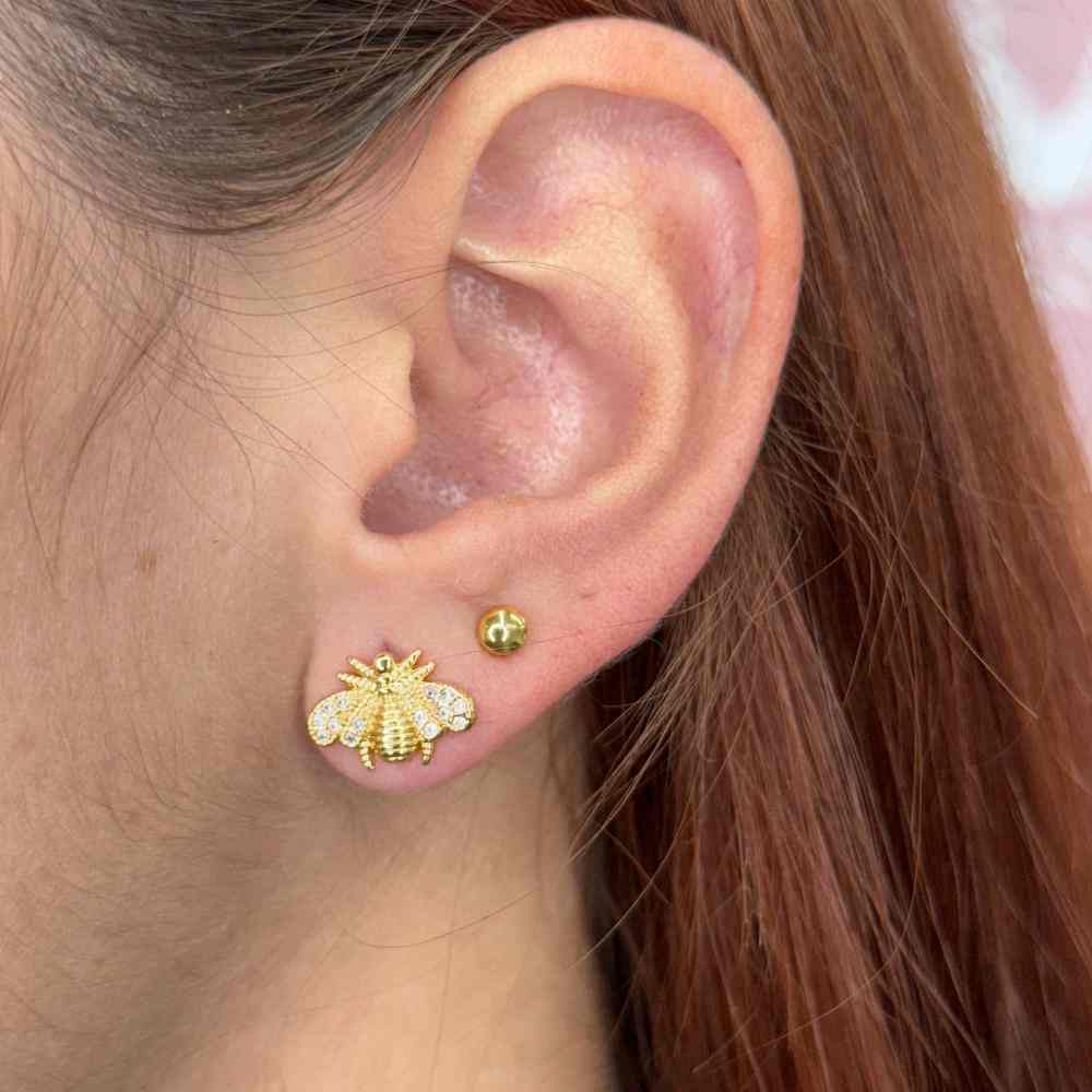 Close-up of ear wearing a gold Stud Fly stud earring with detailed bee design alongside a small gold round stud.