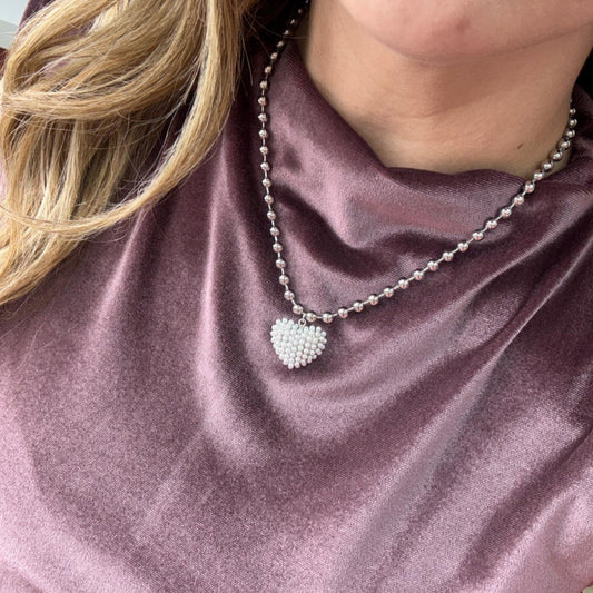 Close-up of a stainless steel Love Pearl Chain with pearl heart pendant worn on a purple satin top
