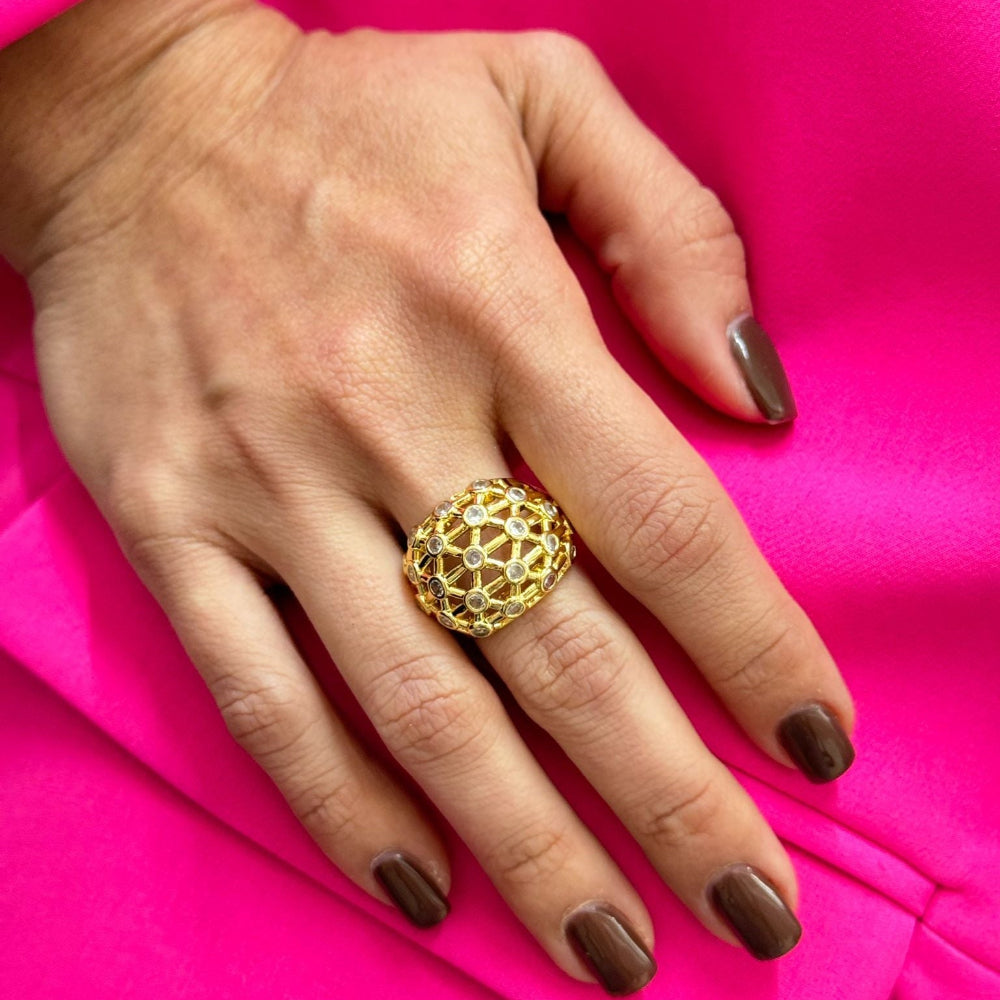 Hand wearing a gold SHINE DOME RING with sparkling pave stones on a bright pink fabric background