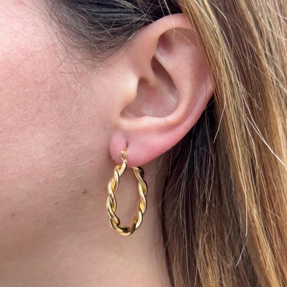 Close-up of a gold twist hoop earring worn on a woman's ear, showcasing its elegant twisted design and polished finish.