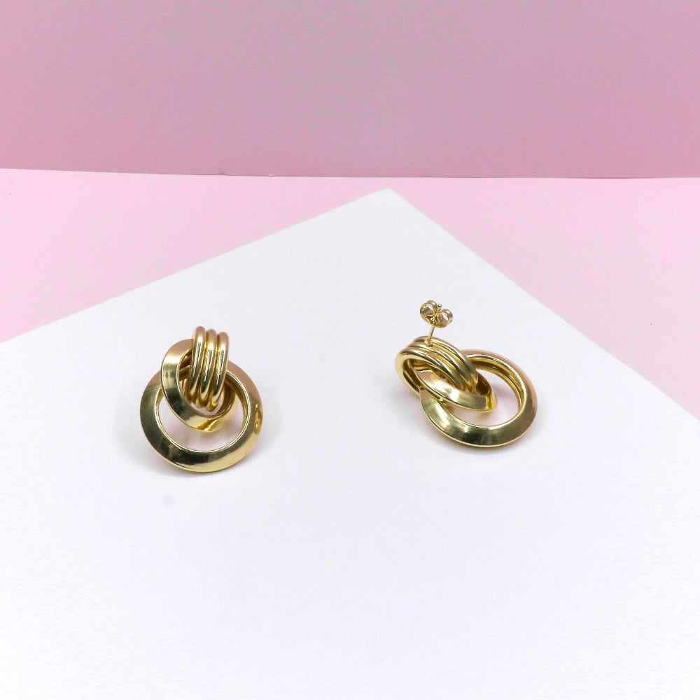 Gold abstract rings earrings with modern twisted design on white and pink background