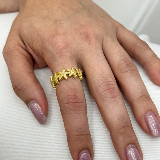 Hand wearing a gold ring with pink nail polish on a white background