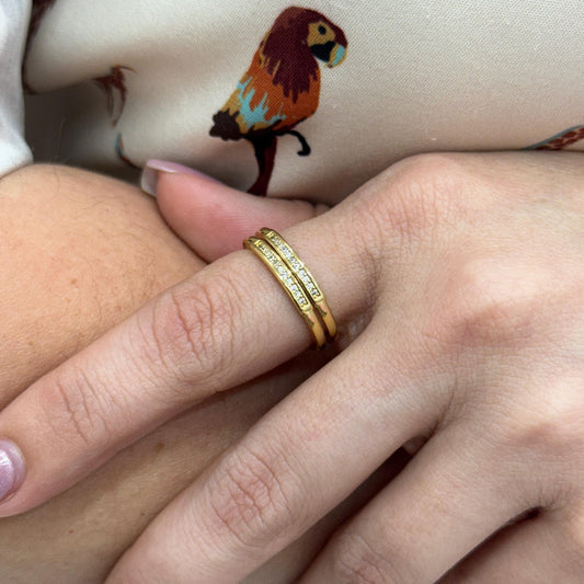 Gold ring on a finger with a colorful bird design in the background
