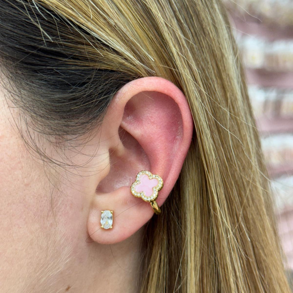 Close-up of an ear wearing gold and pink floral earrings with a blurred background.