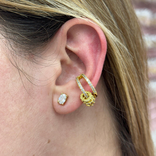 Close-up of an ear wearing gold hoop earrings with clear gemstones.