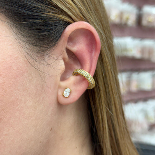 Close-up of a person's ear wearing gold hoop earrings with a blurred jewelry store background.