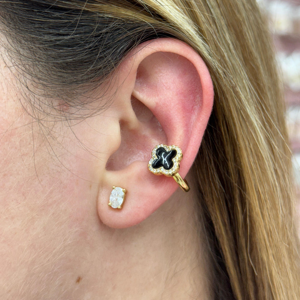 Close-up of a person wearing gold earrings with black clover designs.