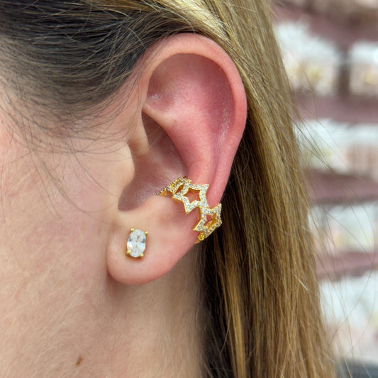 Close-up of an ear wearing gold and clear gemstone earrings with a blurred background.