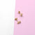 MINI SQUARE STUD earrings on a pink and white background.