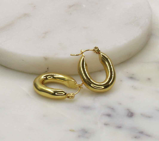 Gold oval earrings made from stainless steel on a marble surface.