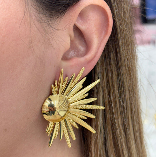 Close-up of a gold Sunshine Earring with radiating spikes worn on the ear.