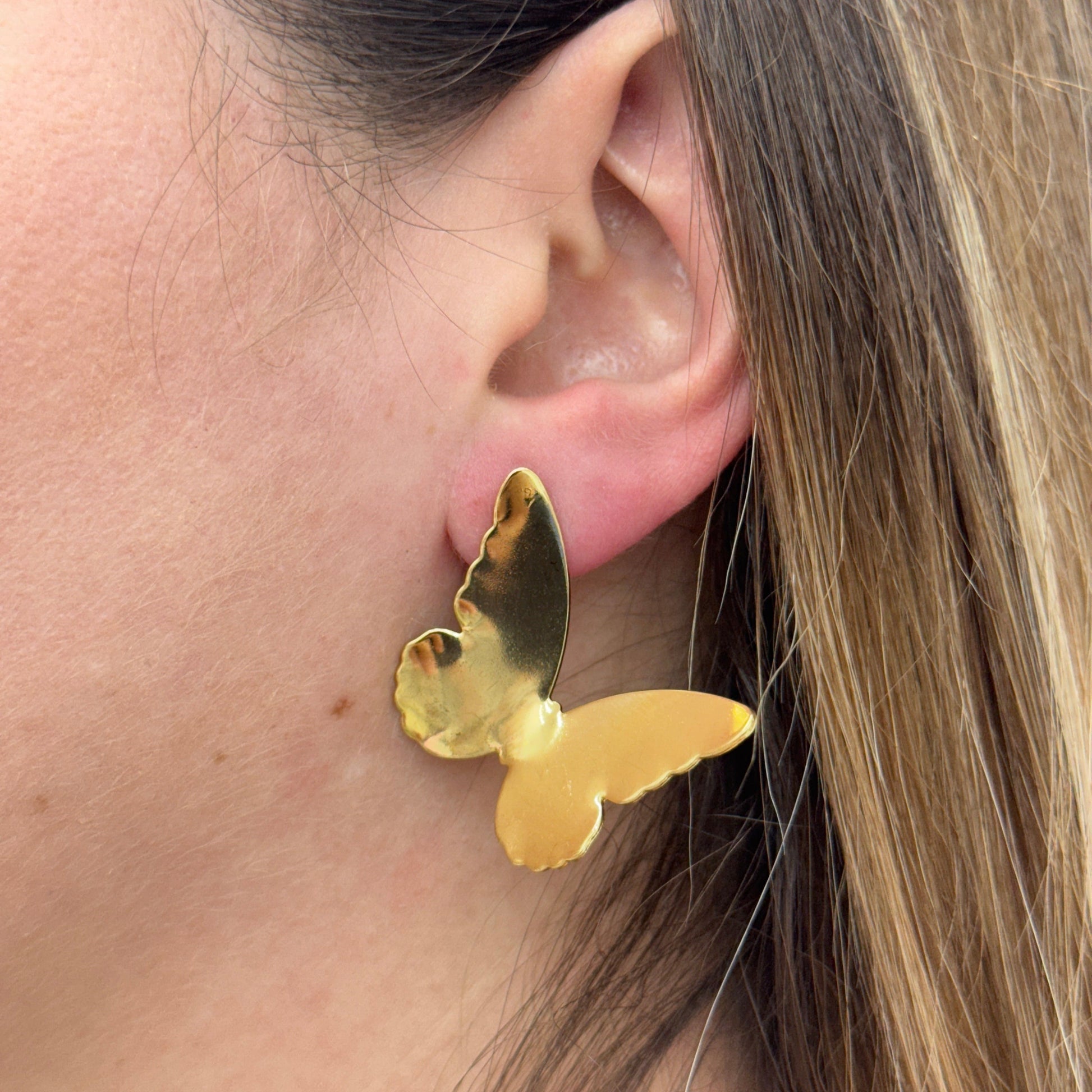 Close-up of a gold stainless steel butterfly earring worn on an ear