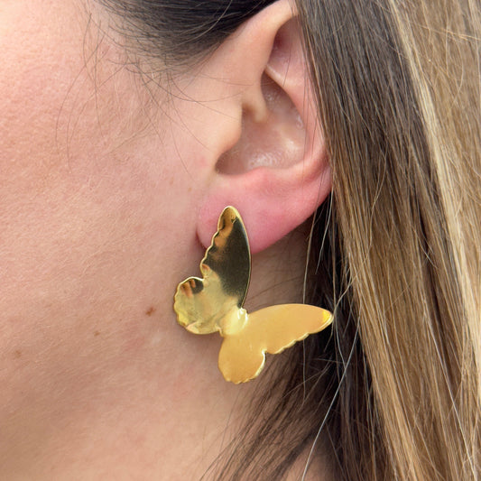 Close-up of a gold stainless steel butterfly earring worn on an ear