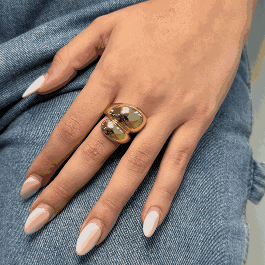 Hand wearing adjustable double drop style gold ring on denim background
