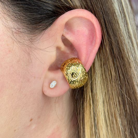 Close-up of a gold textured COCO EARCUFF worn on the upper ear with a small diamond stud earring on the earlobe.