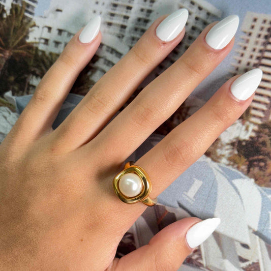 Gold-colored Mother Pearl Ring with a central pearl on a hand with white nails.