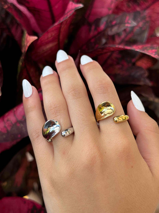 Hand wearing three FLAT GOTA GOLD & SILVER RINGs with modern design against dark red foliage background