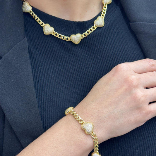Gold-filled Cuban link chain and bracelet set with textured heart accents on a person wearing a black top and blazer