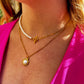 Close-up of a woman's neck wearing a luxurious pearls layering chain with gold clasp and a gold pendant necklace, styled with a bright pink top.