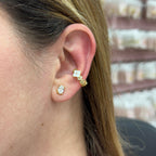 Close-up of an ear wearing gold and diamond earrings with a blurred jewelry display in the background.