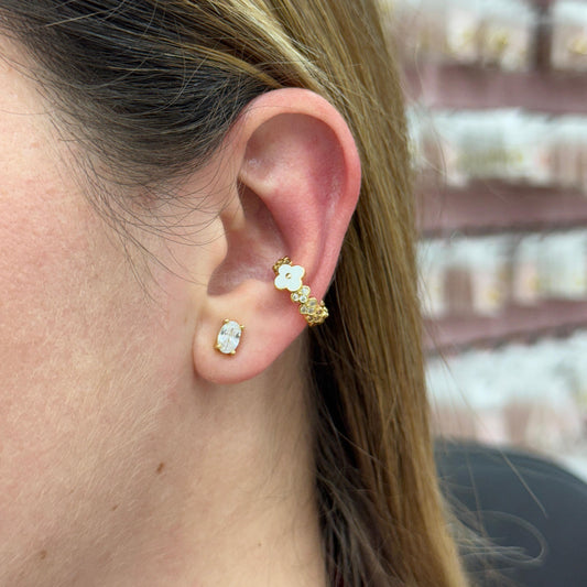 Close-up of an ear wearing gold and diamond earrings with a blurred jewelry display in the background.